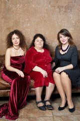 Elderly mother and two daughters sit on old leather couch in room with frayed walls.