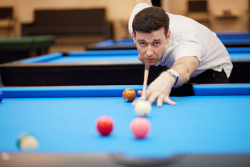 Man aims white ball with cue stick on pool table in club.