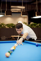 Man in white polo-neck shirt plays pool in club.
