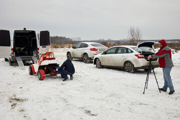 Cameraman shoots man prepares buggy car for training outdoor on winter day.