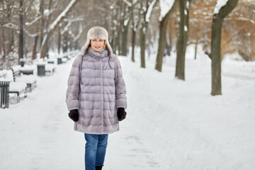 Woman in fur coat and hat walks in winter park.