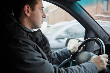 Man seats on driver seat at steering wheel in modern car on winter day, profile view.