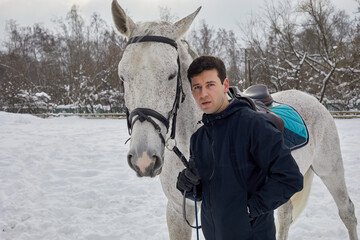 Man stands in park with white horse on winter day.