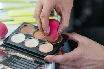 Close up view of a person holding makeup palette and sponge.
