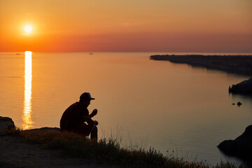 Man sits on seashore on summer sunset.