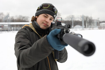 Boy with gun takes aim during lasertag game outdoor at winter day near railway station