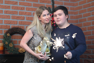 Woman with doll and her son teenager with sparkler pose in room with christmas tree