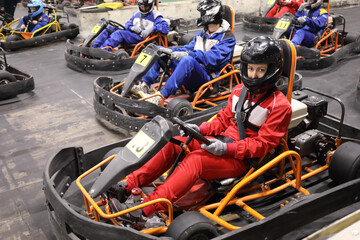 Four adults and two children prepare for driving karting, focus on right woman in red - obrazy, fototapety, plakaty