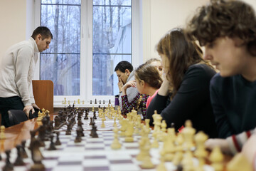 Six people (adults and children) play chess on table in chess club