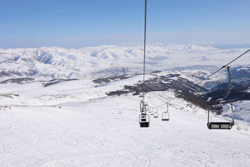 Fototapeta na wymiar Empty cableway at winter day in Cahkadzor resort in mountains; Hrazdan town far away