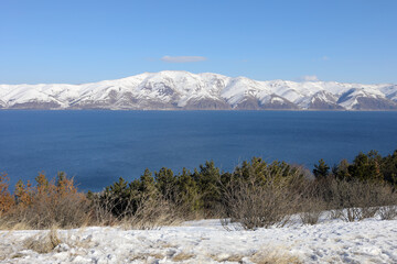 Blue Sevan lake and beautiful snowy mountains at winter sunny day in Armenia