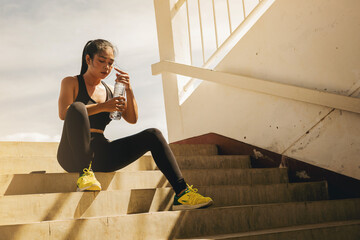 Tired runner woman with a bottle of electrolyte drink freshness after training outdoor workout at the stadium stairway