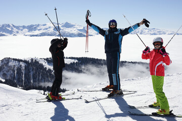 Father, son, daughter skiers in ski goggles stand with raised arms on mountain in ski resort at...