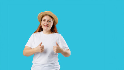 Young happy 30s Caucasian woman in hat isolated on blue background giving a thumbs up and good luck gesture, studio portrait. Human emotions, facial expression concept