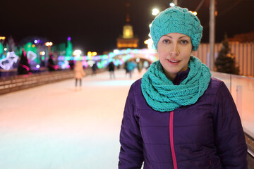 Happy woman stands on ice rink outdoor at night, shallow dof