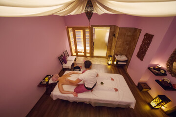 Massage therapist does thai massage for woman on couch in spa room, top view