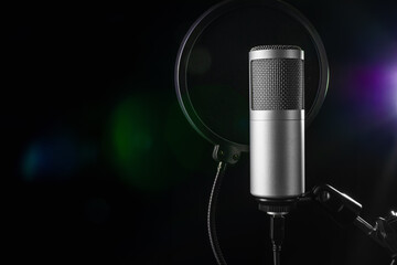Studio microphone with a pop filter, poised for an audio recording session, set against a dark backdrop illuminated by colorful lights.