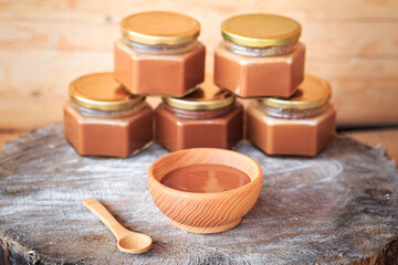 Boiled condensed milk in a wooden plate, close-up against the background of glass jars filled with condensed milk, food photography, wooden background.