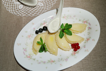 Five dumplings with berries and sour cream on plate on table
