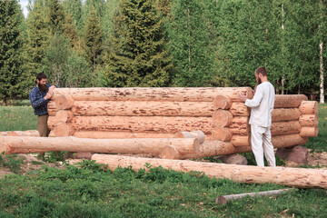 Two men are building a wooden house from logs in nature, logs in the foreground, construction, village, summer, greenery, forest, bathhouse, carpenters, peasants.