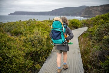 Woman and toddler hiking in the Tasmanian wilderness in the bush under the mountain and above the water camping in the wild with a backpack in Australia