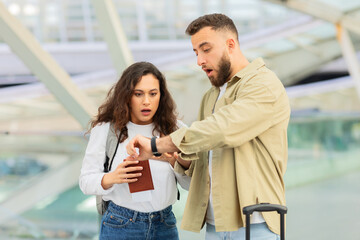 Stressed Young Couple Late For Flight, Standing At Airport And Checking Wristwatch