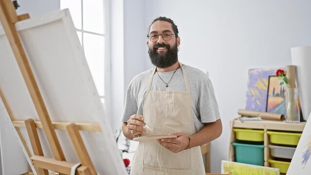 Handsome bearded man painting on canvas in bright art studio, showcasing creativity and artistic skill indoors.