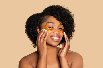 Joyful black woman with golden under-eye patches, skin care routine