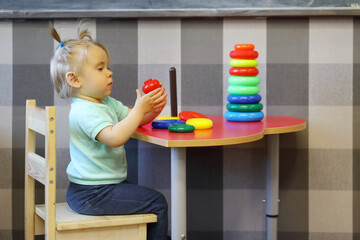 Little girl plays with stacking toy on table in modern kindergarten