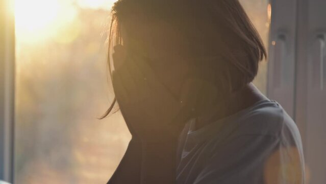 Regretful unhappy mid adult female by the bedroom window, sunlight shining through with intentional lens flare