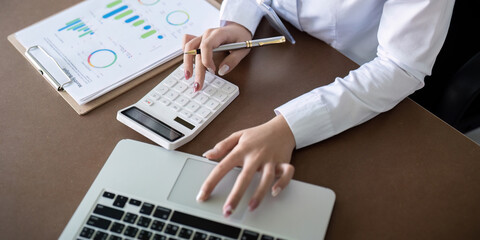 Finance concept. Close up businesswoman hold a graph pen and writing report, and memo, and analyzing business documents with a laptop computer