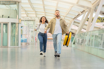 Determined couple sprinting through airport corridor with suitcase, trying to catch flight