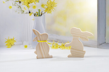 Easter bunnies made of wood stand on the windowsill with a bouquet of flowers