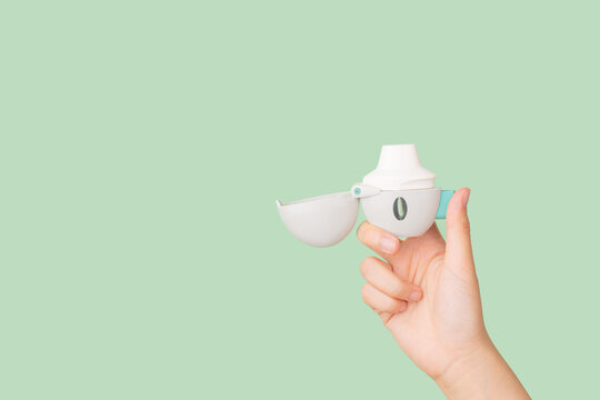 Asthma and COPD concept. Female hand holding Tiotropium bromide  inhaler on green background. Pharmaceutical device of bronchodilator for lung inflammation treatment and prevent asthma attack.