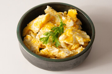 Fresh breakfast scrambled eggs inside a dark ceramic bowl in a clean white background