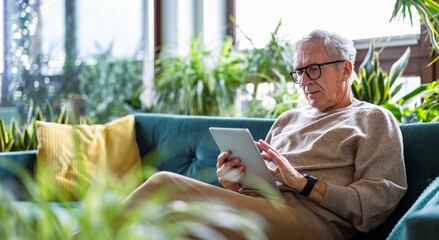 Senior man using digital tablet while sitting on sofa in living room at home
