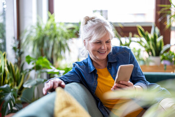 Smiling senior woman using smart phone while sitting on sofa at home
- 762349902