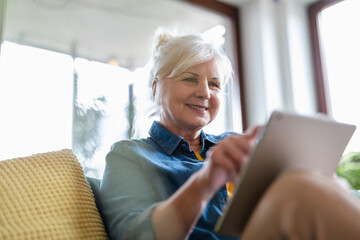 Mature woman using digital tablet while sitting on sofa at home
