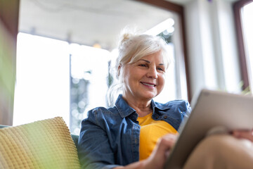 Mature woman using digital tablet while sitting on sofa at home
