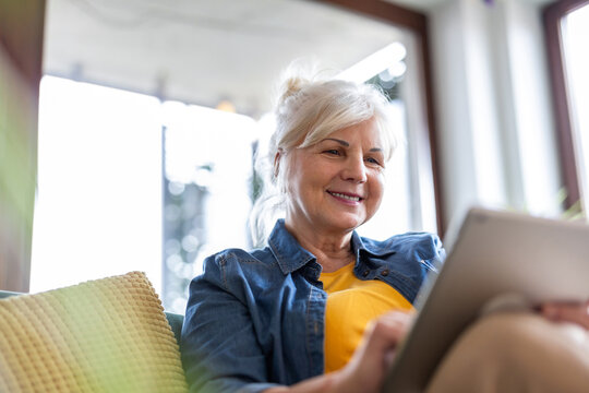 Mature woman using digital tablet while sitting on sofa at home
