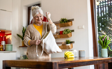 Senior woman holding reusable bag with groceries in kitchen
