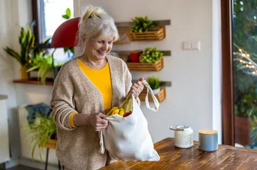 Foto op Plexiglas Senior woman holding reusable bag with groceries in kitchen  © pikselstock