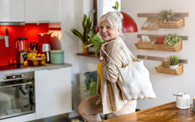 Senior woman holding reusable bag with groceries in kitchen
- 762350133