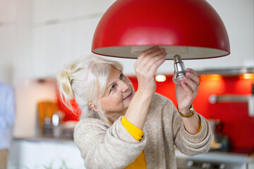 Senior woman changing light bulb in her home
