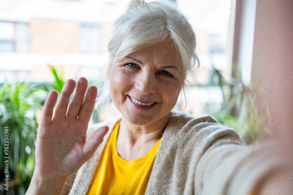 Poster Portrait of smiling senior woman taking selfie with mobile phone at home
