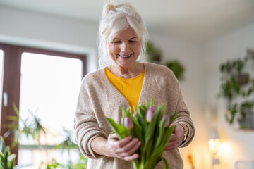 Happy senior woman with bouquet of tulips in vase at home
- 762350310