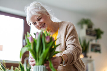 Happy senior woman with bouquet of tulips in vase at home
