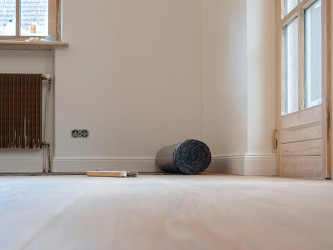 Expansive apartment room during renovation, featuring wooden floors covered with gray malervlies painter's fleece for protection against painting and work.