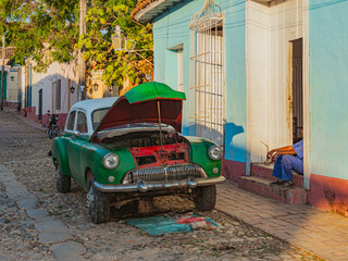 Vintage classic American car get repaired on street. Repair works with engine of an old american car. Old American car being repaired on a town street. Sity Life on Cuba, Trinidad