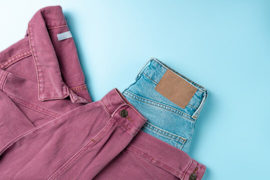 Pink denim jeans jacket with blue jeans, on blue background. Fashion concept. Flat lay, top view